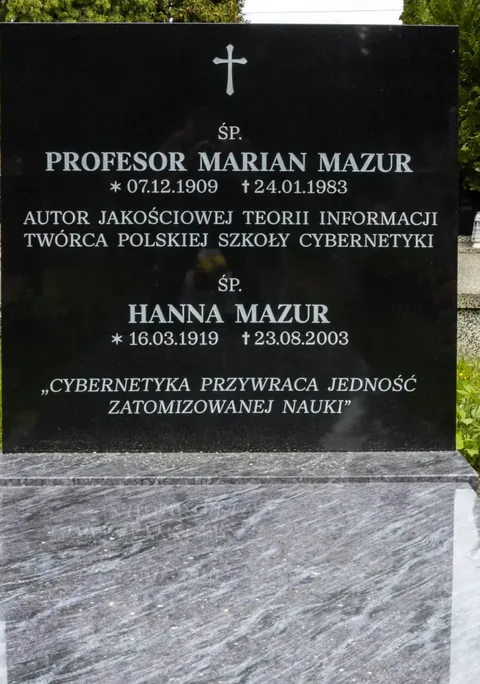彩色照片:黑色花岗岩墓碑,碑文为“Profesor Marian Mazur, autor jakościowej teorii informacji, twórca Polskiej Szkoły Cybernetyki”(马里安·马祖尔教授,定性信息论的作者,波兰控制论学派创立者),并刻有引文“控制论恢复了被原子化的科学的统一”。
